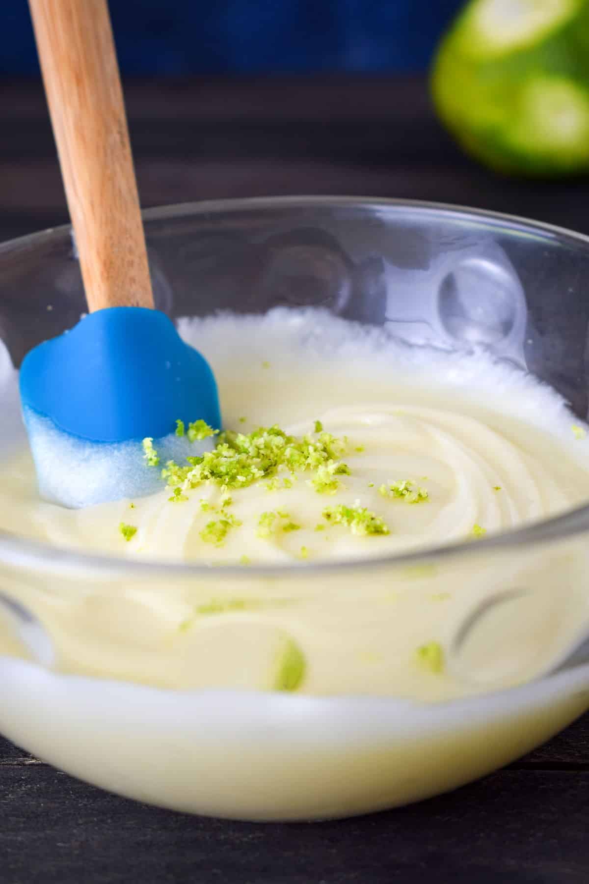 Cream cheese frosting for cake pops in a bowl with lime zest on top.
