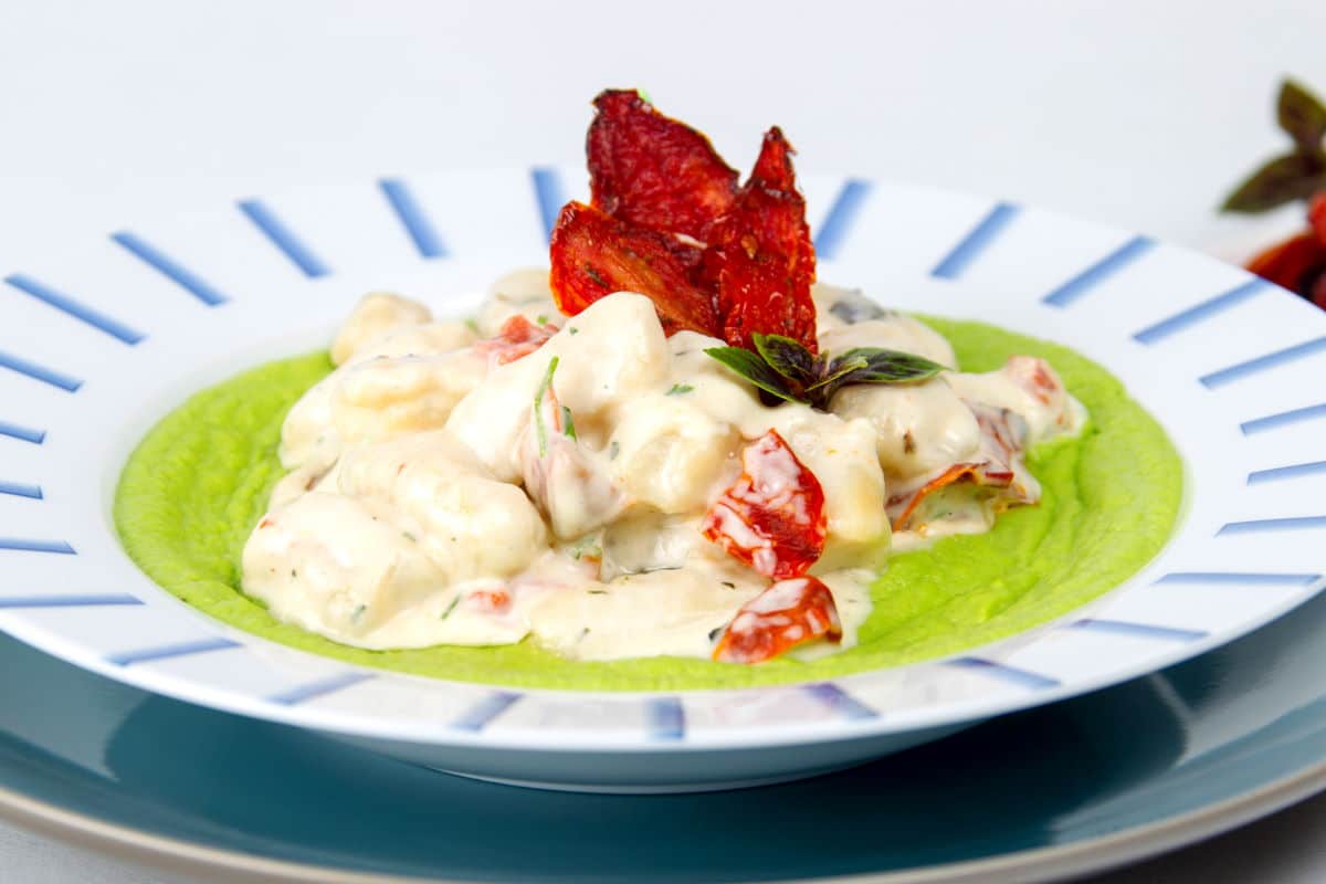 Gnocchi and pea puree with sundried tomatoes in dish.