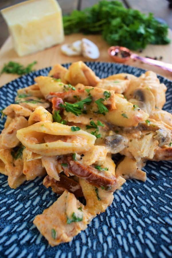 Creamy tuna casserole on a blue plate with Parmesan, parsley and mushrooms in the background.