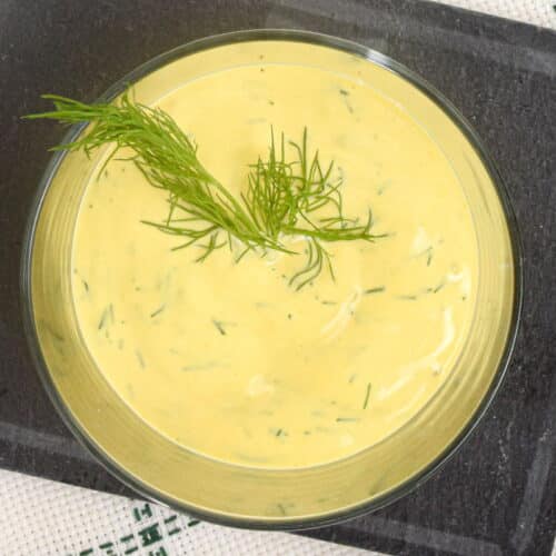 Dill dip in a glass serving dish with a fresh dill sprig.