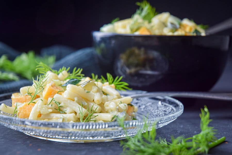 Dill pickle pasta salad garnished with fresh dill on a clear glass plate, dark background.