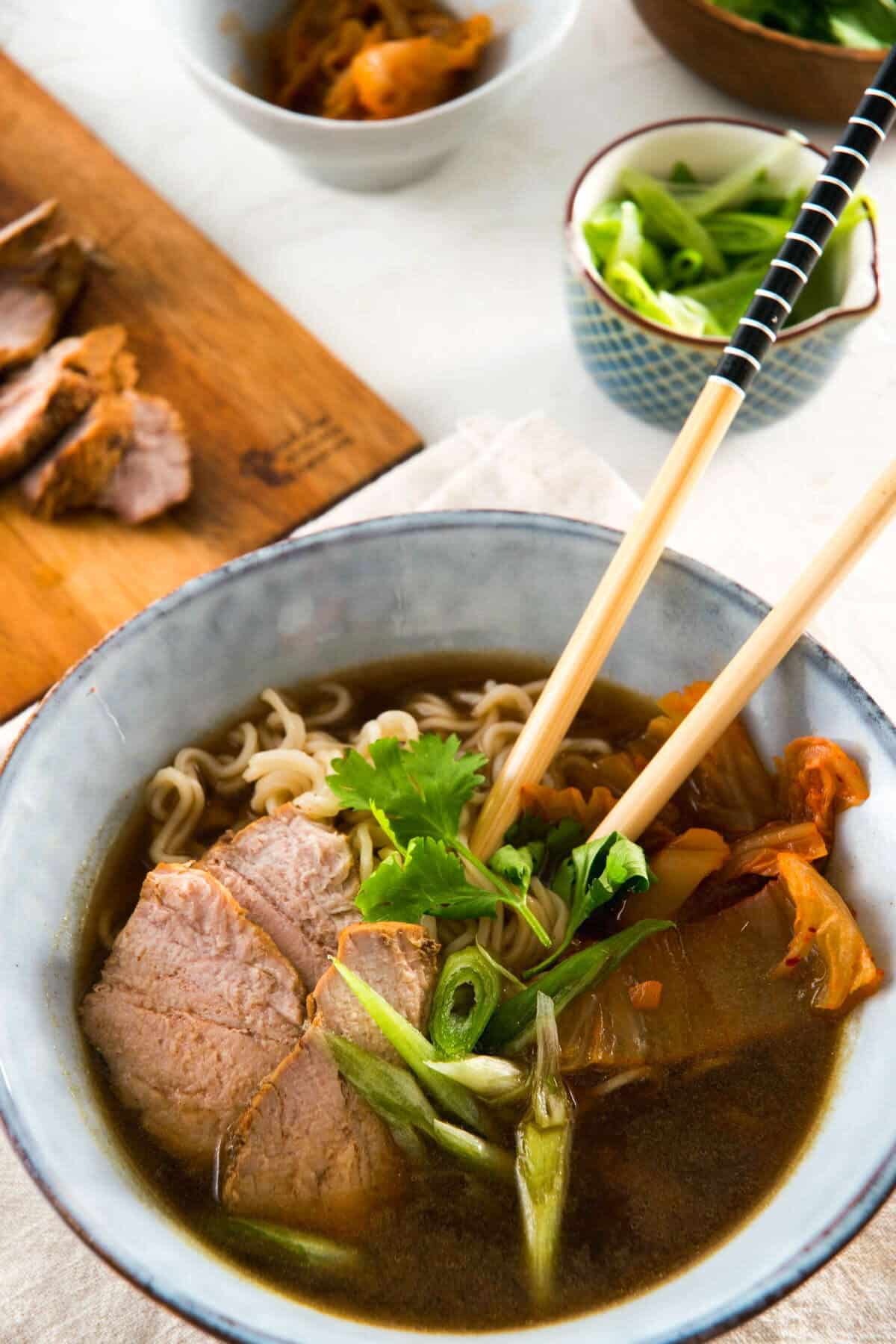 Kimchi ramen with pork slices and chopsticks in a bowl.