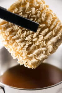 Instant ramen noodles in a pot with tongs.