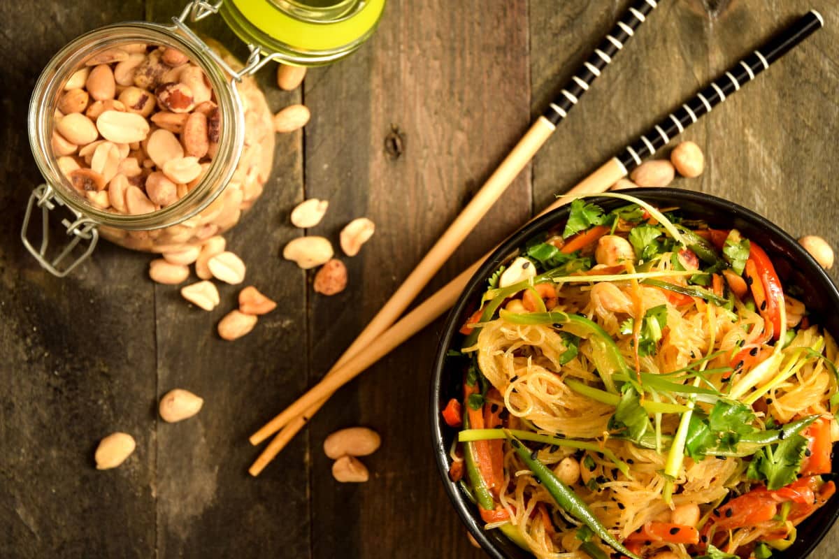 Vegan Pad Thai in a black bowl with chopsticks and peanuts in a jar on the side.