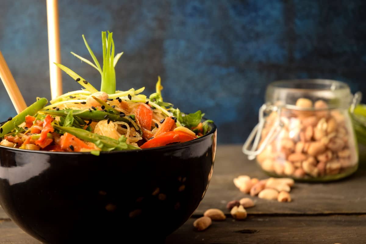 Vegan Pad Thai in a black bowl with peanuts in a jar in the background.