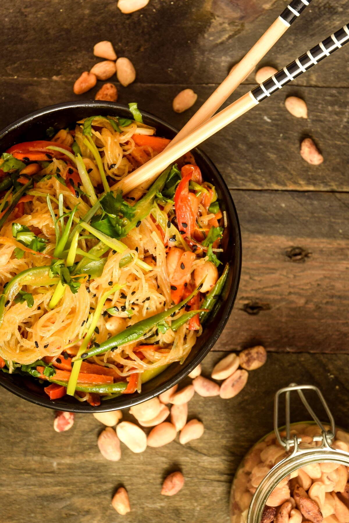 Top view of Pad Thai in a black bowl with chopsticks and peanuts on the side.