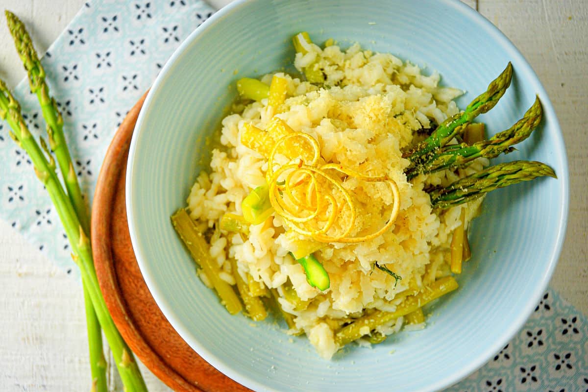 Top view of risotto with lemon and asparagus in light blue bowl.