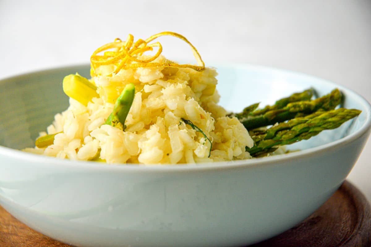 Risotto with lemon and asparagus in light blue bowl.