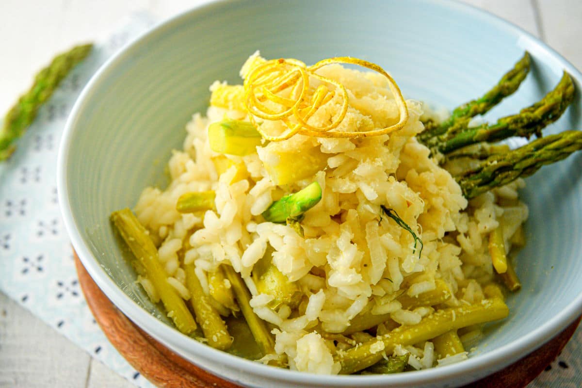 Close up of risotto with lemon and asparagus in light blue bowl.