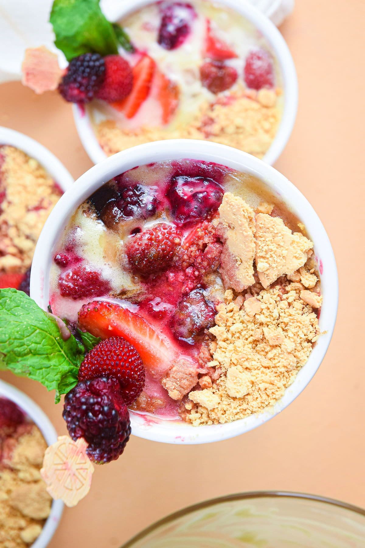 Berries and cream in a ramekin with fresh mint and crumbled cookie.