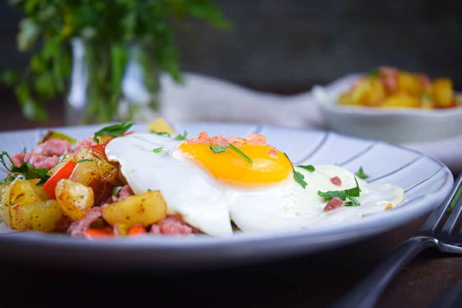 Electric skillet sausage and egg breakfast hash on a plate with a fork on the side, dark background.