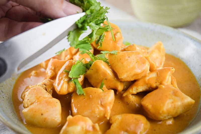 Electric Skillet Butter Chicken in a bowl with parsley, light wooden background.