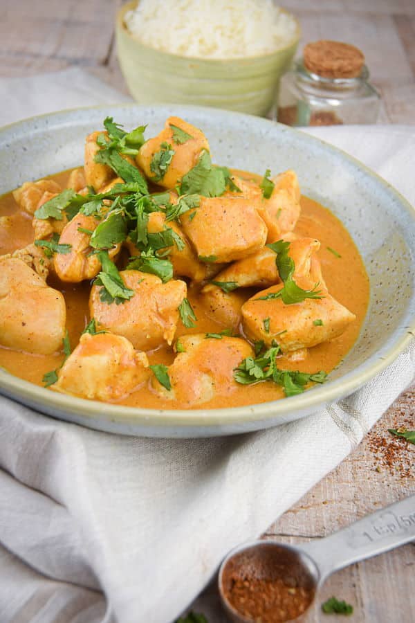 Electric Skillet Butter Chicken in a bowl with rice on the side, light wooden background.