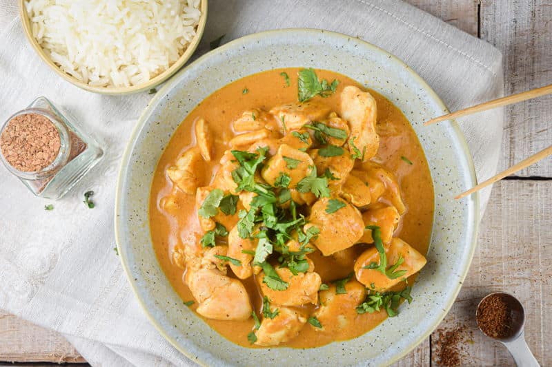 Electric Skillet Butter Chicken in a bowl with rice on the side and chopsticks, light wooden background.