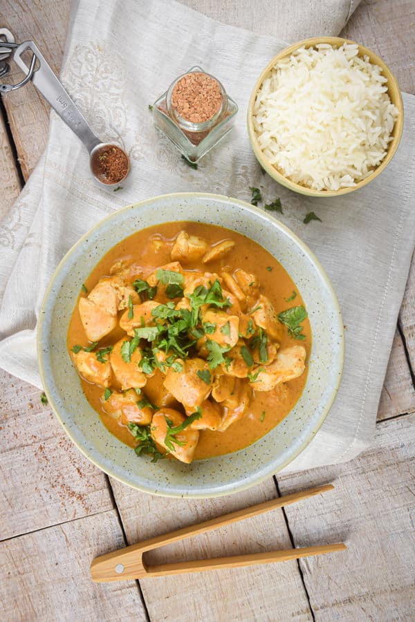 Electric Skillet Butter Chicken in a bowl with rice on the side and chopsticks, light wooden background.