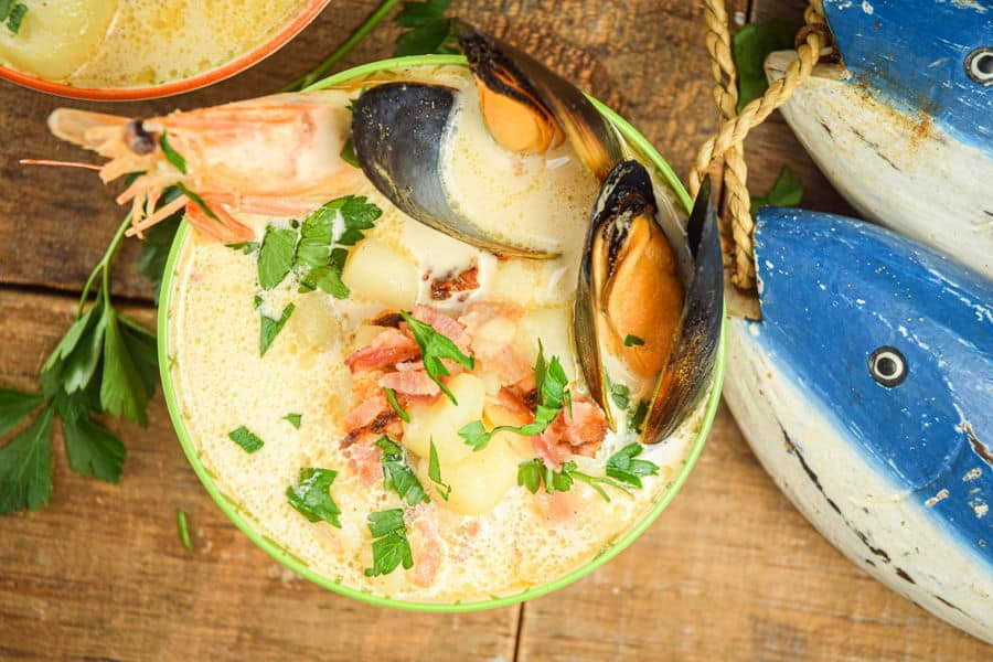Electric Skillet Seafood Chowder in a bowl, wooden background, wooden fish decoration on the side.