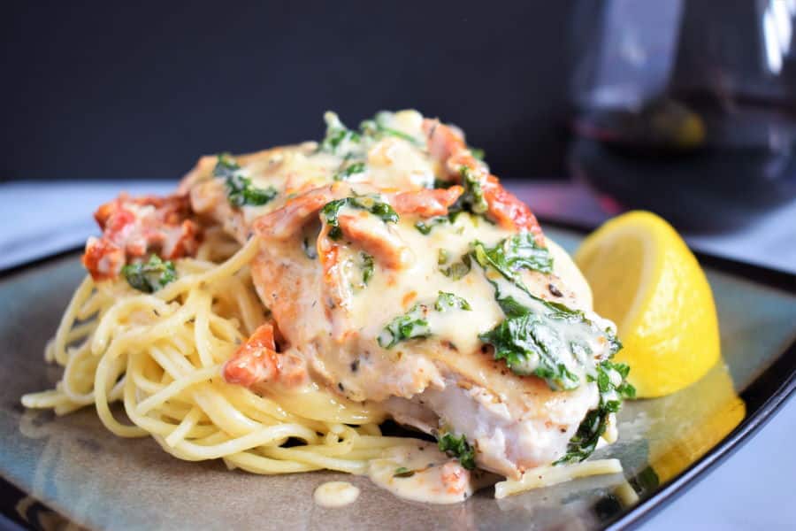 Creamy tuscan chicken and lemon wedge on a plate, dark background, red wine on the side.