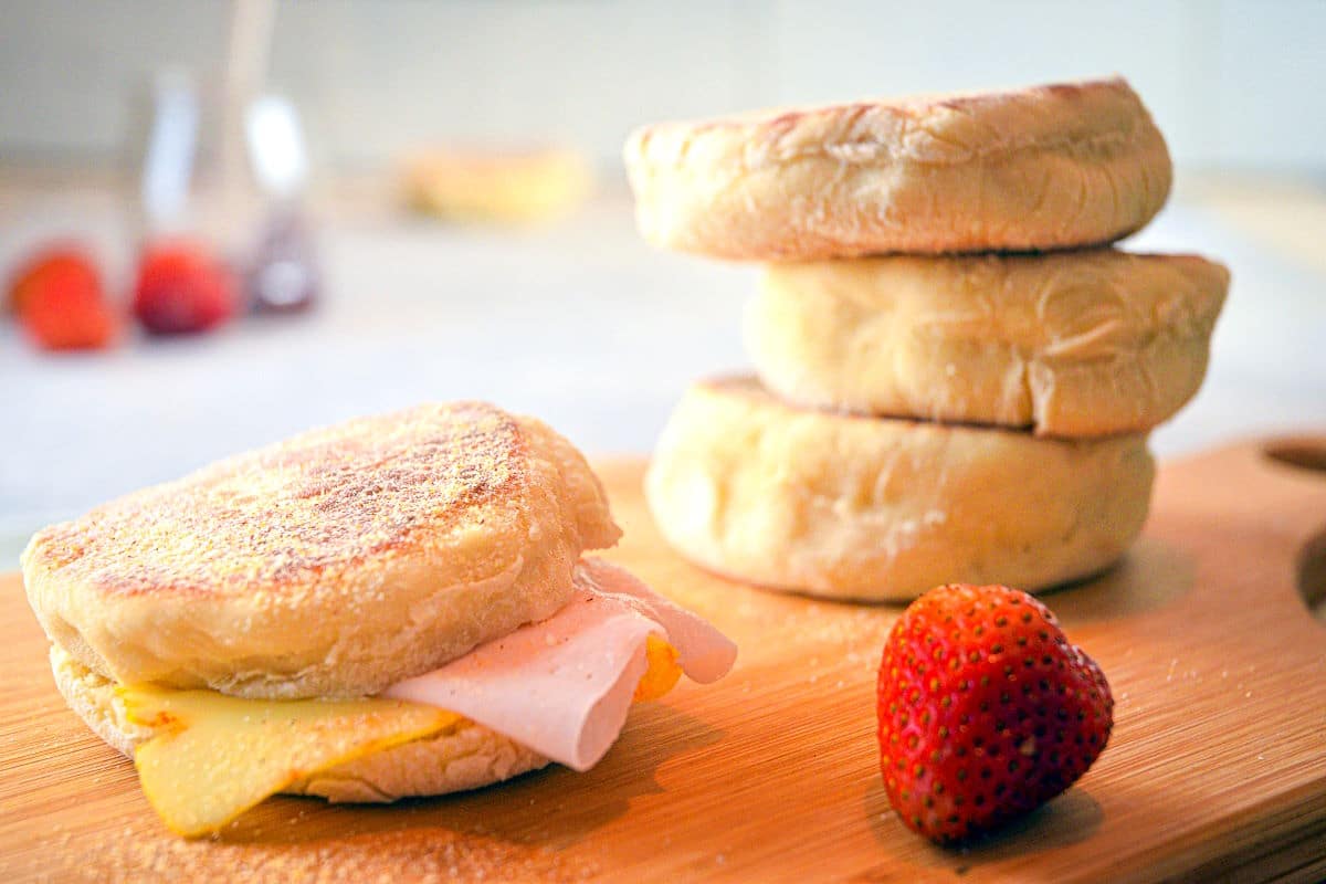 English muffin with ham and melted cheese and a strawberry on the side.