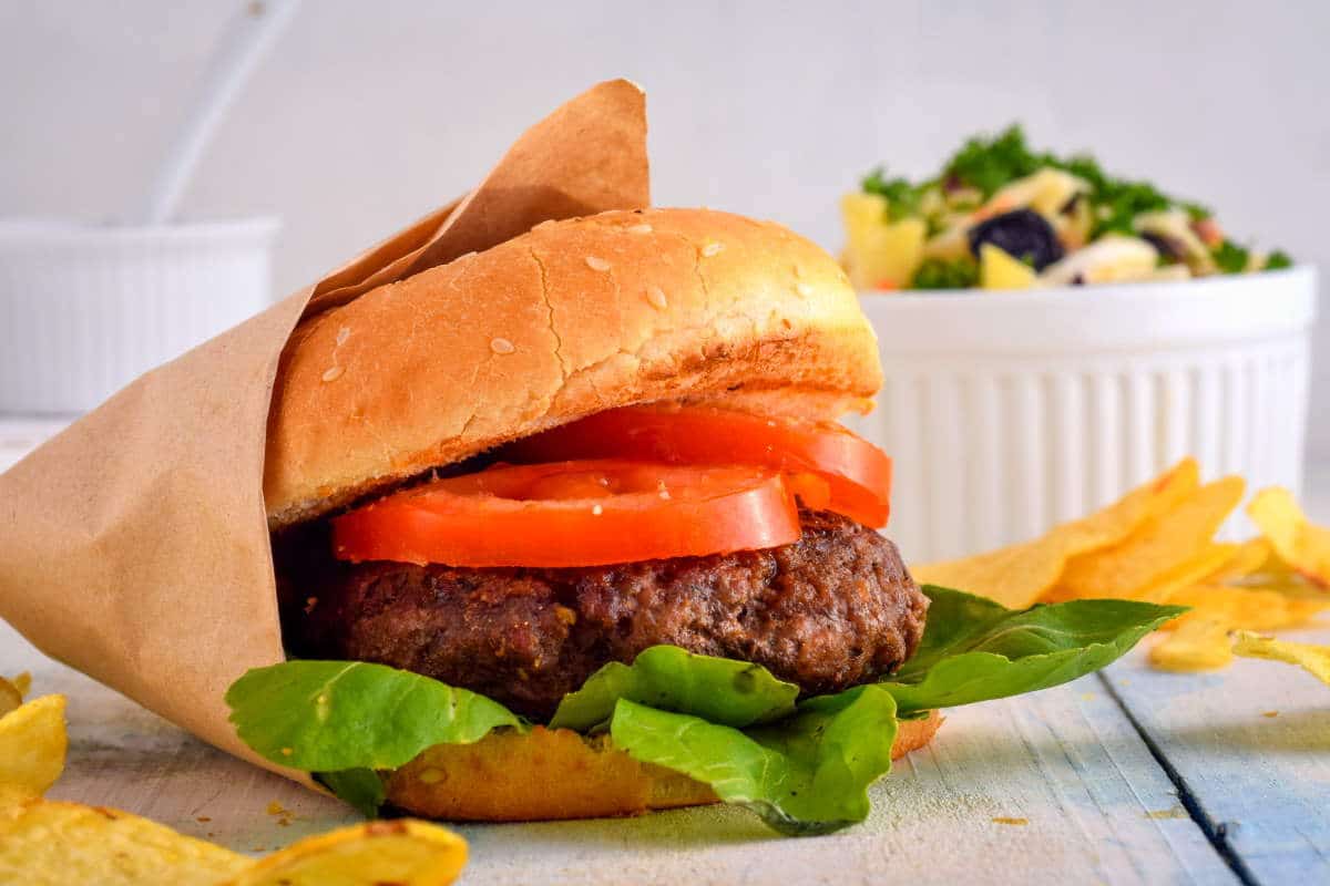 Electric Skillet Hamburgers on wooden background with salad and condiments on the side.