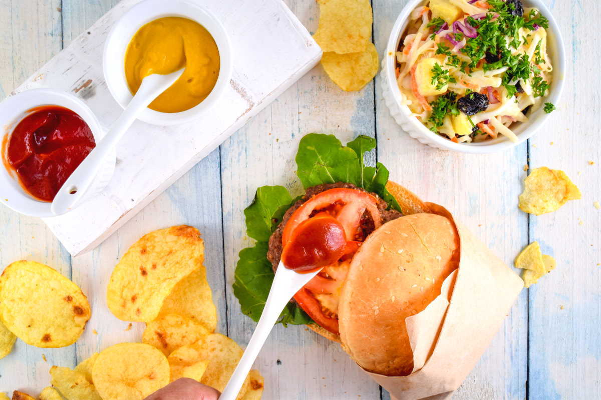 Electric Skillet Hamburgers on wooden background with salad and condiments on the side.