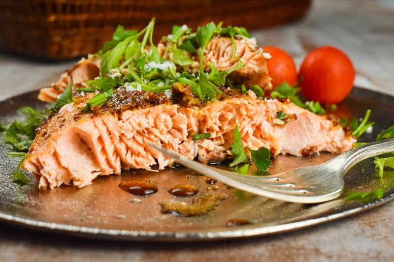 Wild salmon with fresh parsley and tomatoes on a plate with a fork.