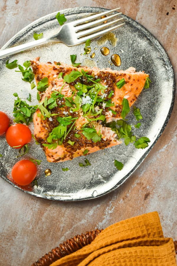 Wild salmon with fresh parsley and tomatoes on a plate with a fork and yellow dish towel.