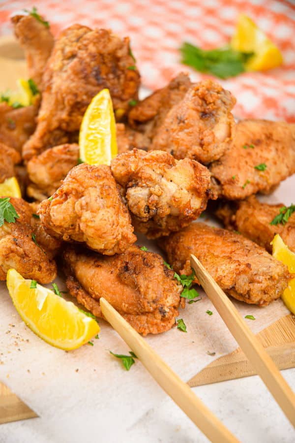 Lemon pepper chicken wings with lemon wedges on wooden cutting board.