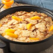 Peach cobbler in an electric skillet on grey background.