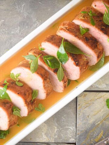 Sliced pork tenderloin in white serving dish with orange white wine sauce.