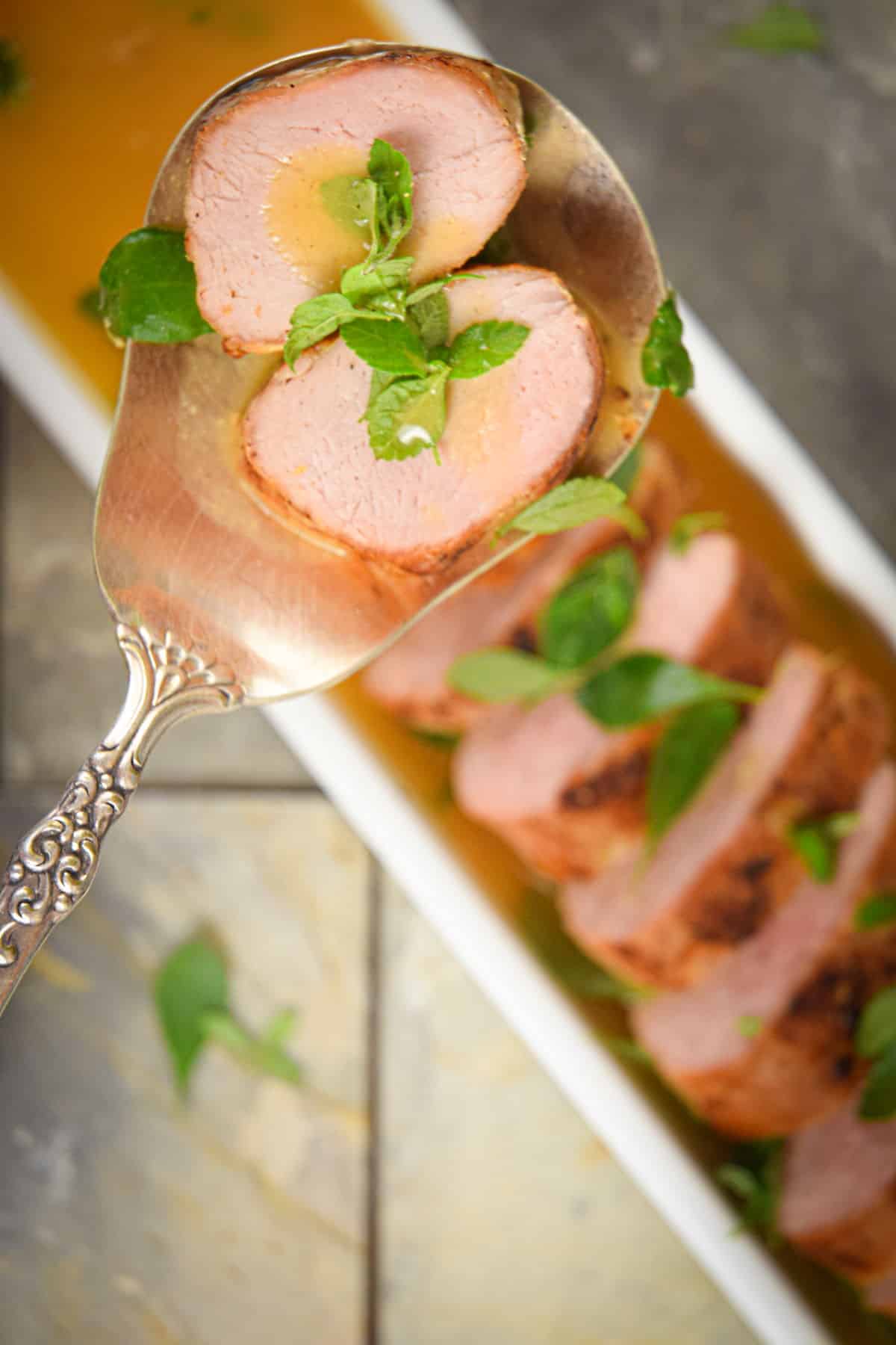 Sliced pork tenderloin in spoon with wine sauce.