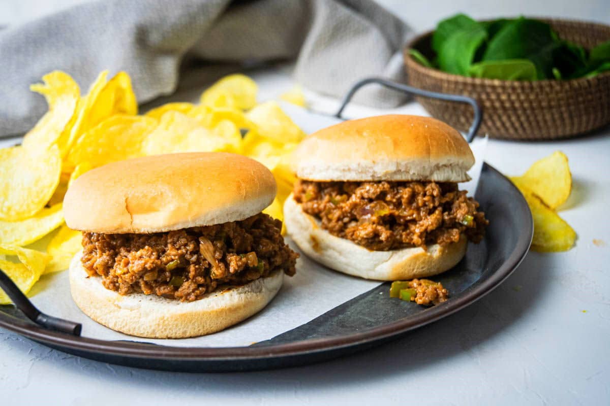 Sloppy Joes on a serving dish with chips and spinach on the side.