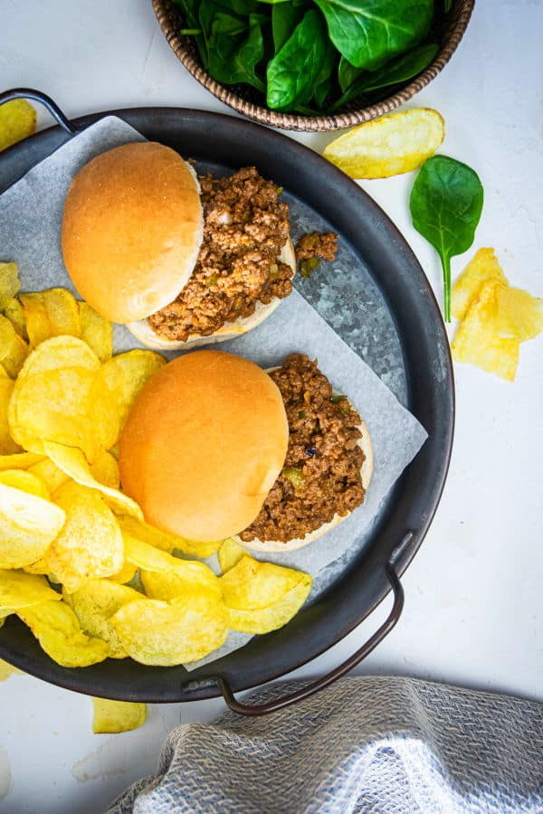 Sloppy Joes on a serving dish with chips and spinach on the side.