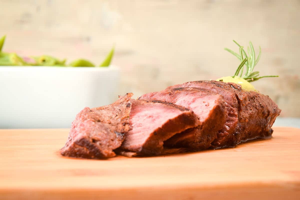 Sliced steak on a cutting board with herb butter.