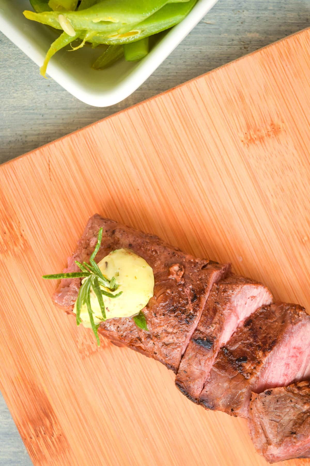 Sliced steak on a cutting board with herb butter.