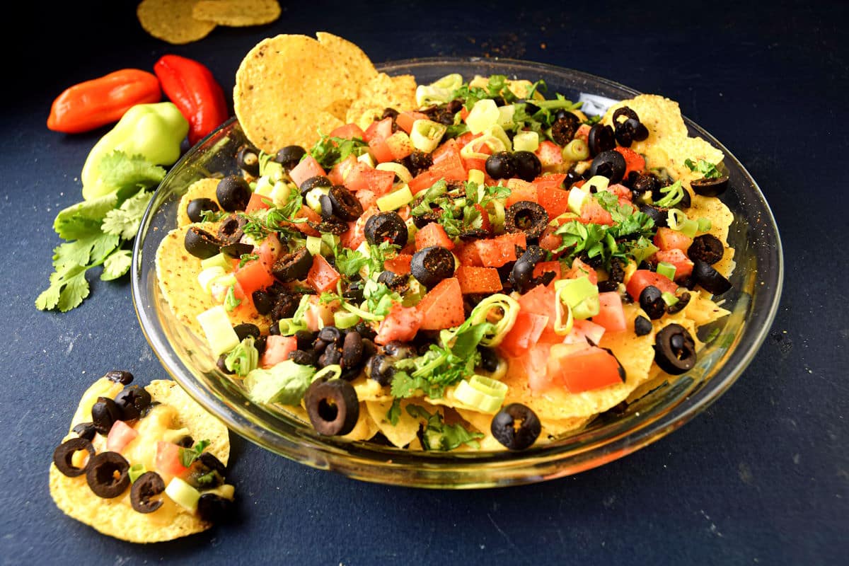 Veggie nachos on a clear glass plate on blue background.