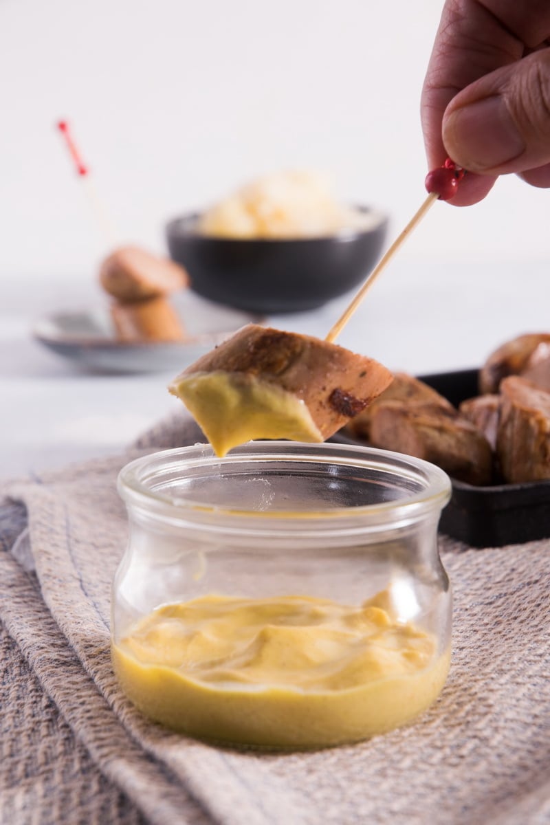 A piece of sausage on a tooth pick with a small jar of mustard dip.