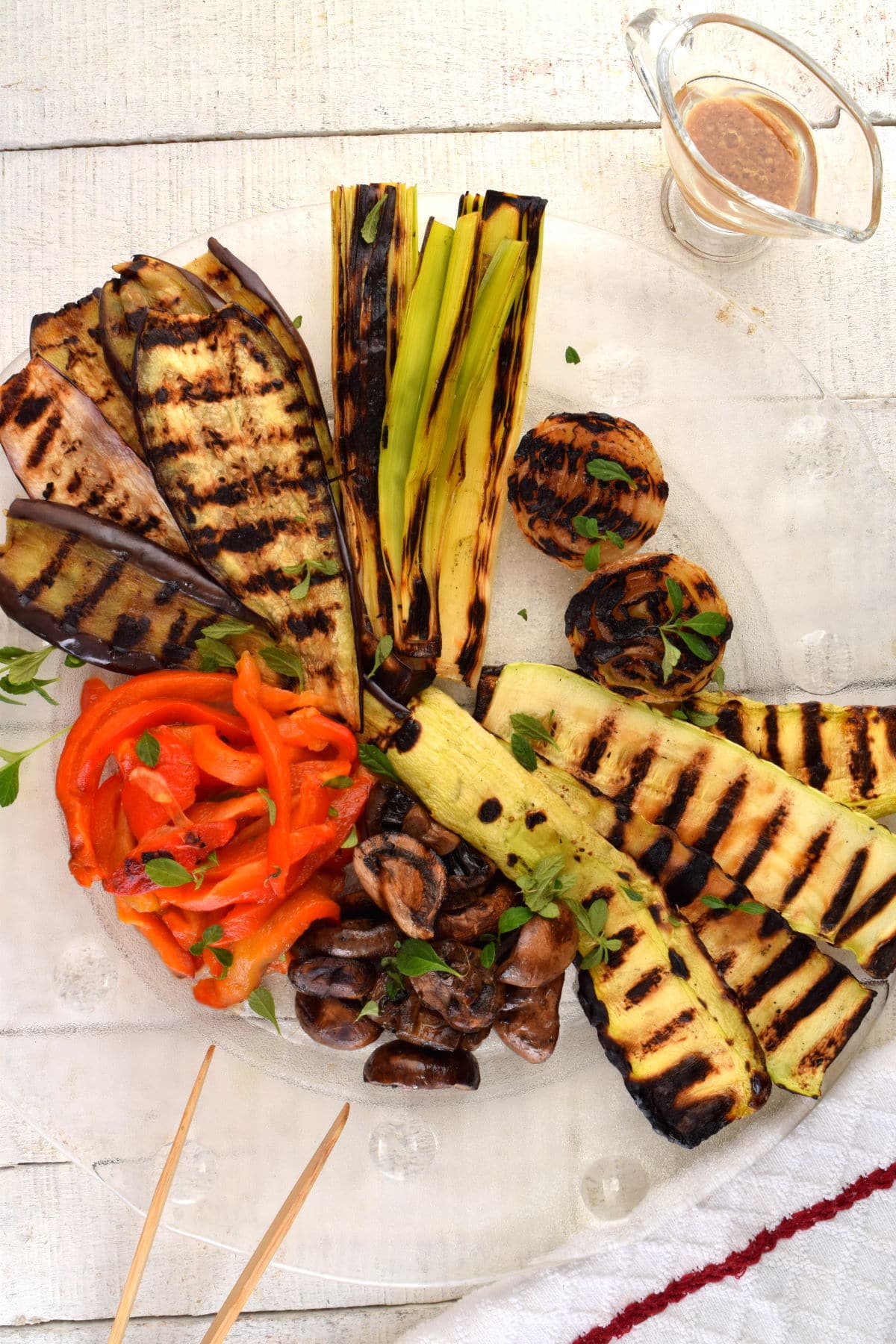 Escalivada grilled vegetables on a plate, with dressing and chopsticks on the side.