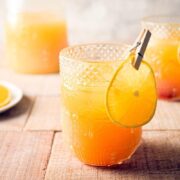 Fall Pumpkin Party Punch in a clear glass with a thin orange slice garnish clipped on with a clothespin, orange slices on a small white plate in the background.