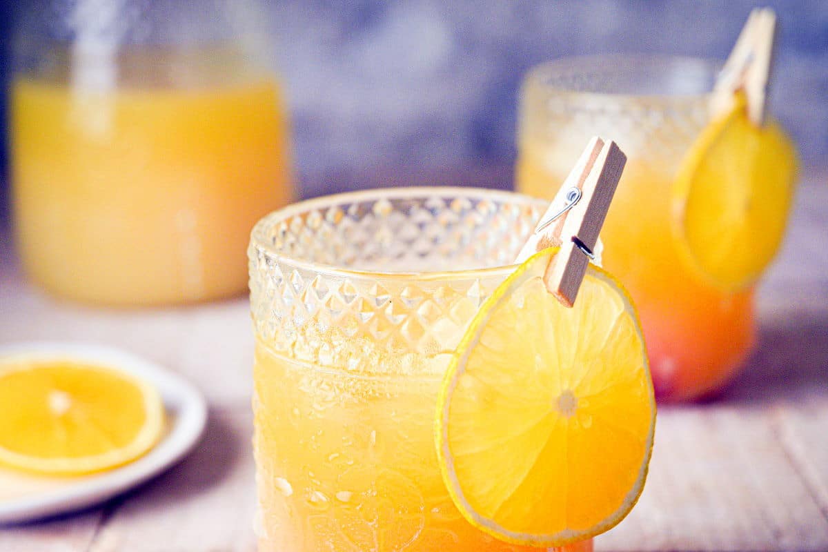 Fall Pumpkin Party Punch in a clear glass with a thin orange slice garnish clipped on with a clothespin.