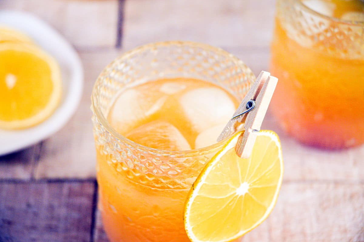 Fall Pumpkin Party Punch in a clear glass with a thin orange slice garnish clipped on with a clothespin.