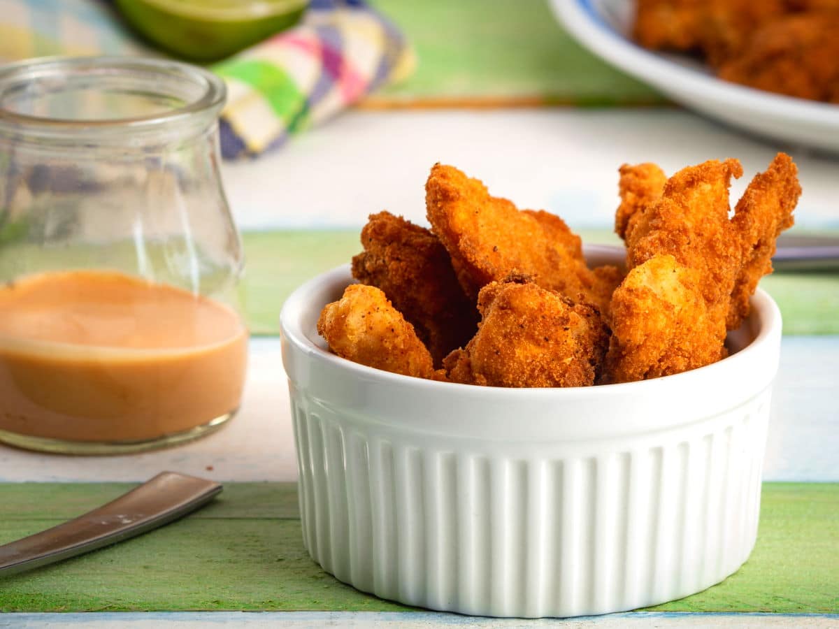 Fish sticks in a white ramekin, dip on the side.