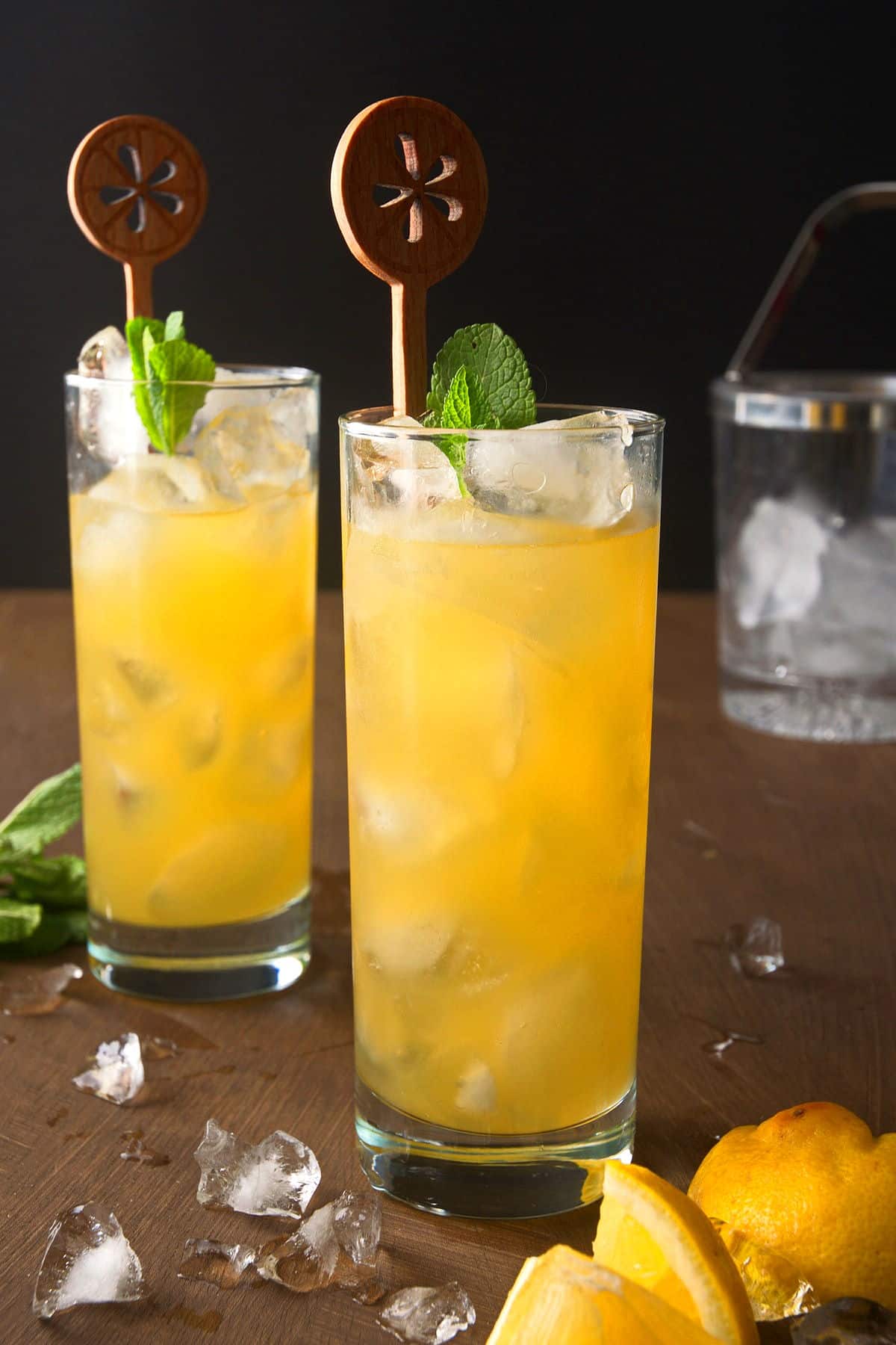 Fog Cutter cocktail in tall glasses with fresh mint, ice and wooden citrus-shaped stirrers.