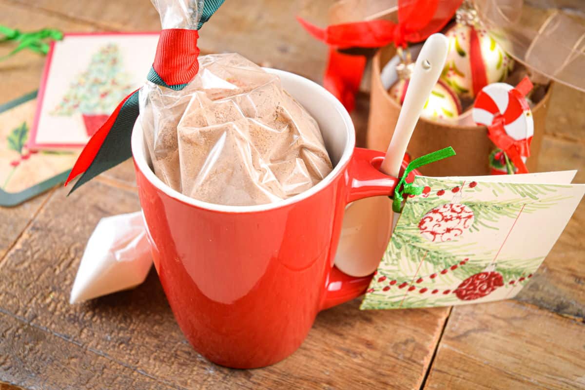 Chocolate cake ingredients in a red mug with Christmas decorations on brown, wooden background.