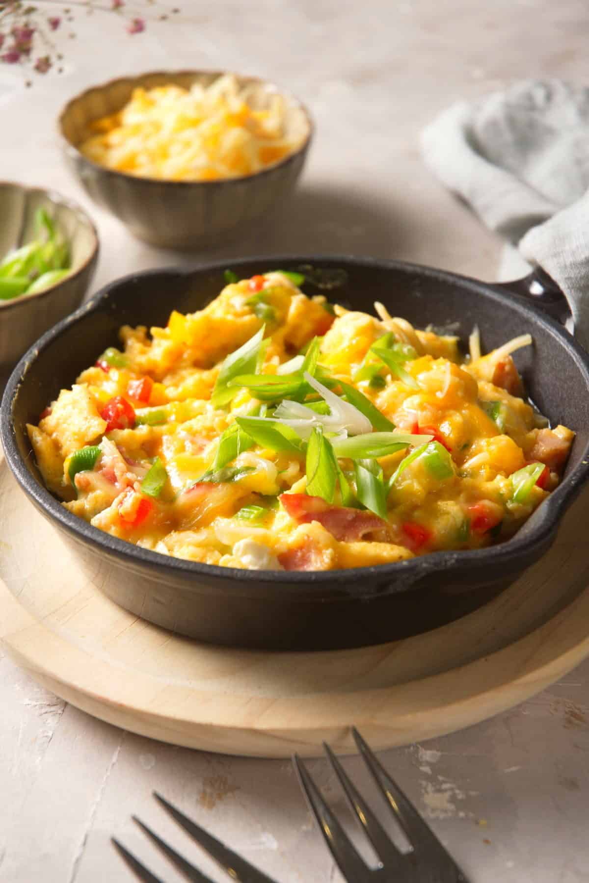 Scrambled eggs in cast iron pan with grated cheese in the background.