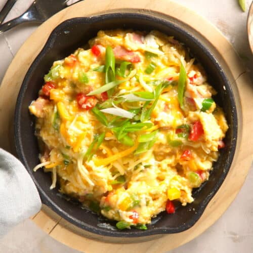 Scrambled eggs in cast iron pan with sliced green onions on the side.