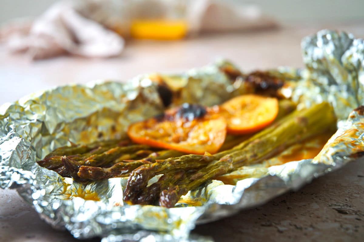 Grilled asparagus with orange slices on foil.