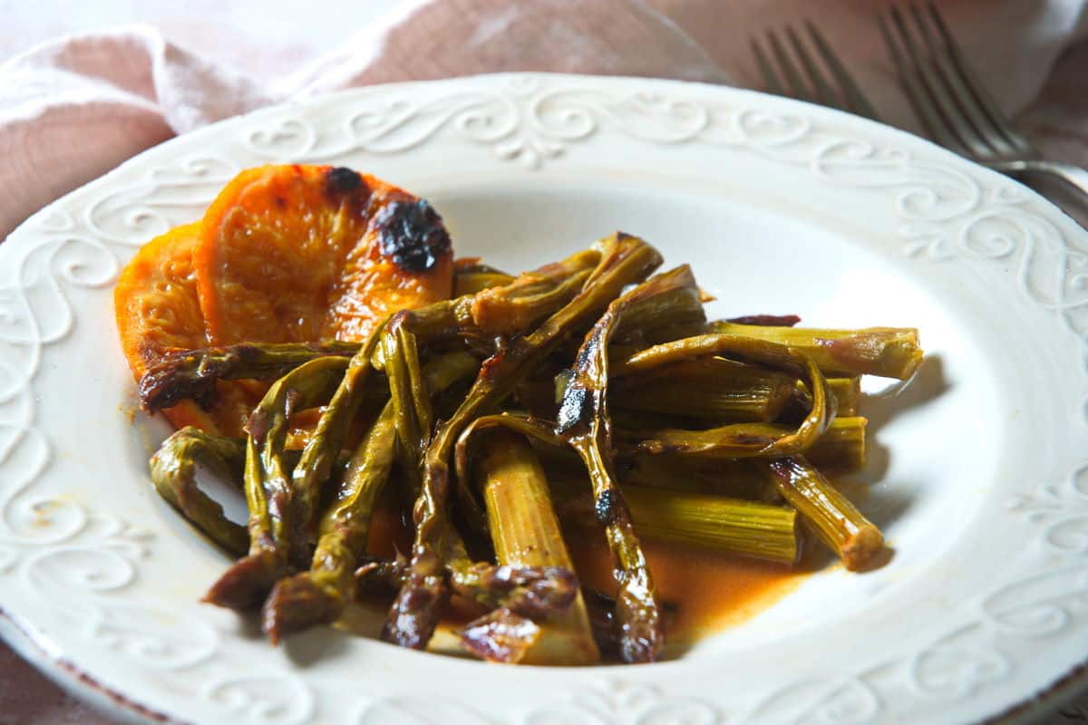 Grilled asparagus with orange slices on white plate.