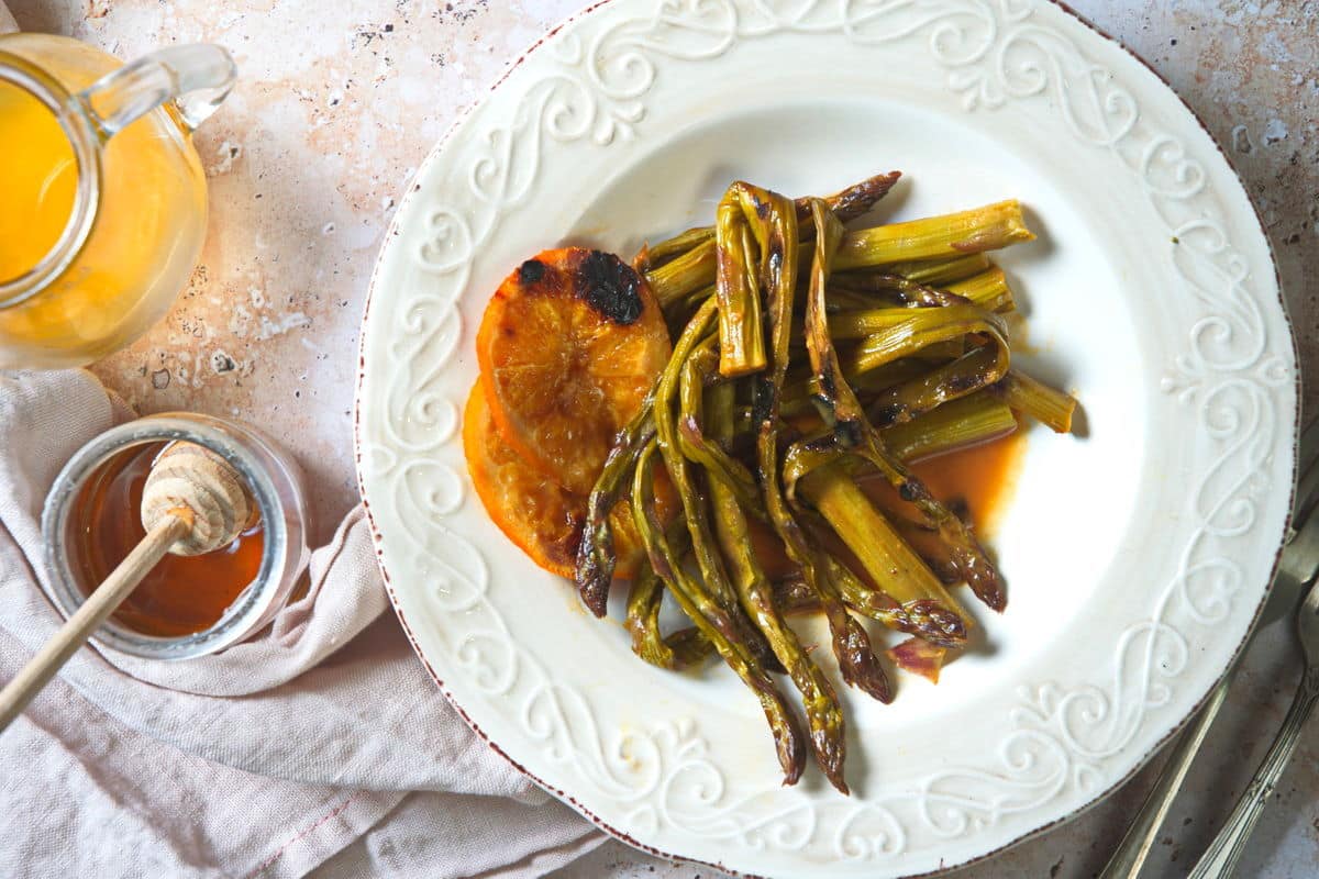 Grilled asparagus with orange slices on white plate. Honey and orange juice on the side.