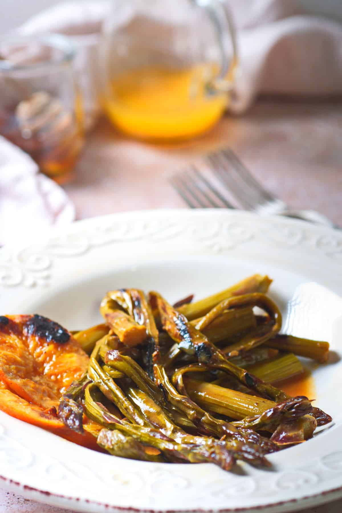 Grilled asparagus with orange slices on white plate. Orange juice in the background.