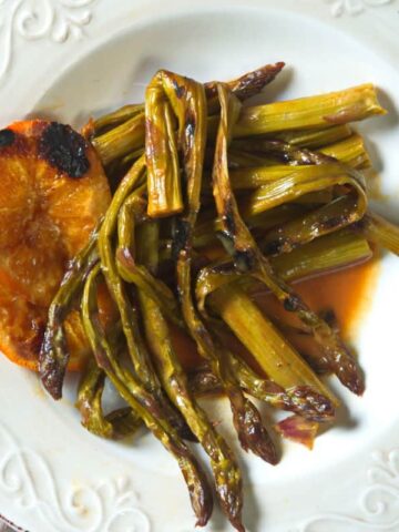 Grilled asparagus with orange slices on white plate.
